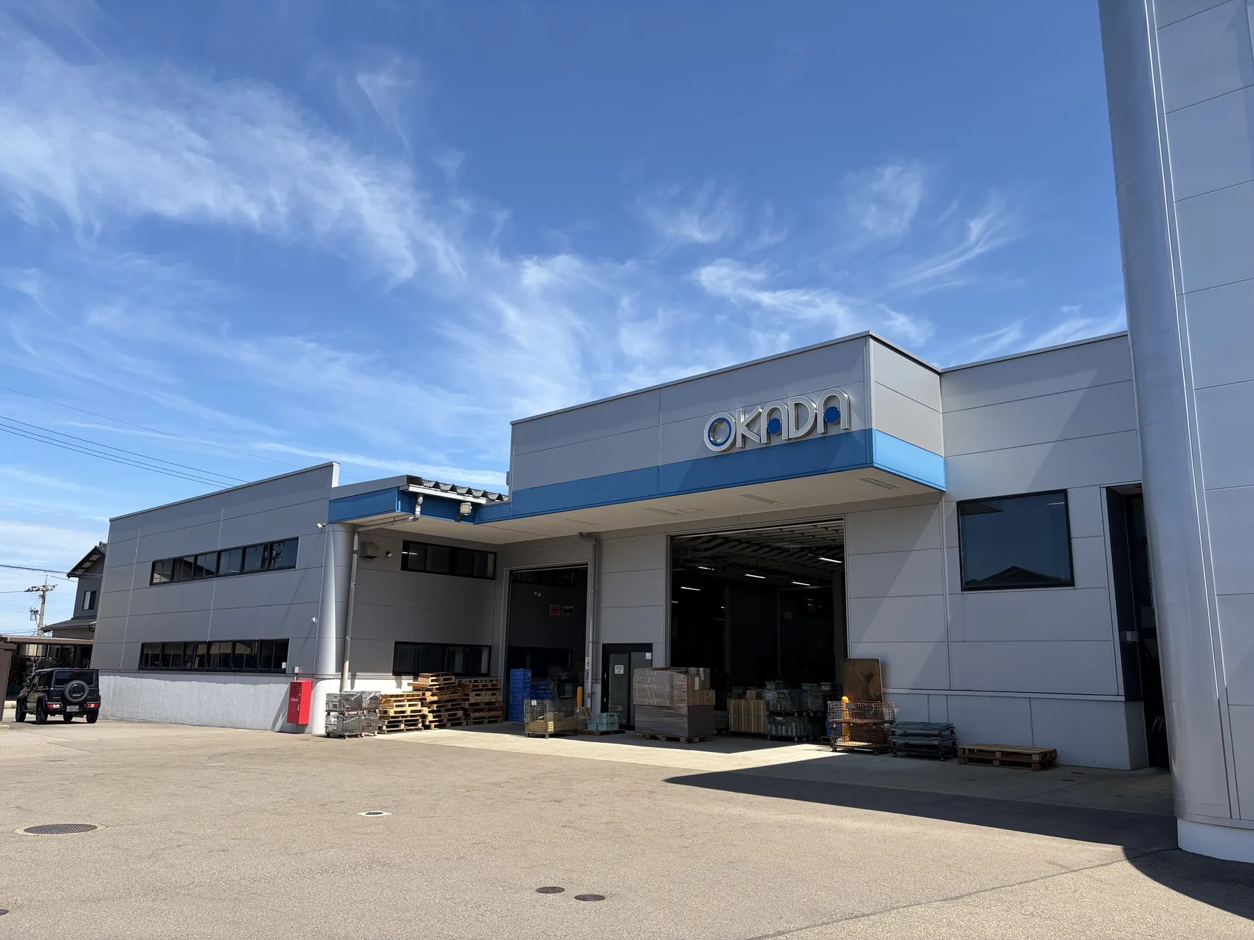 津幡工場の出荷口。青空の下、OKADAのサインを掲げた建物